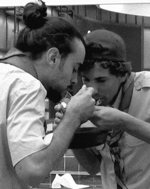 a man with a bun on his head is eating from a bowl next to another man who is eating from a plate