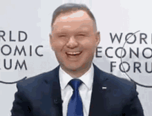 a man in a suit and tie is smiling while standing in front of a sign that says world economic forum .