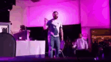 a man is standing on a stage in front of a crowd with purple lights .