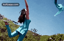 a woman in a blue dress is jumping in the air while a kite is flying in the sky .