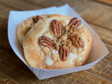 a pastry with pecans on top is in a white paper container