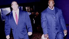 two men in suits and ties are walking down a hallway holding hands .