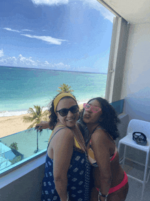 two women are posing for a picture in front of a window overlooking the ocean