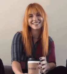 a woman with long red hair is sitting on a couch holding a cup of coffee .