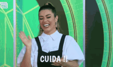 a woman wearing a white shirt and black overalls says cuida