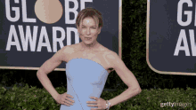 a woman in a strapless blue dress stands on a red carpet in front of a sign that says globe award