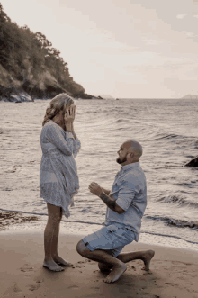 a man kneels down to propose to a woman on a beach