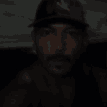 a man with a beard is wearing a hat and looking at the camera in the dark .