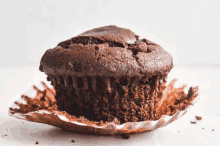 a close up of a chocolate muffin in a paper wrapper on a table