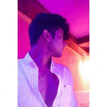 a man wearing a white shirt and a necklace is standing in a room with purple lights .