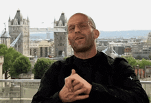 a man wearing glasses and a black jacket is making a funny face in front of a city skyline .