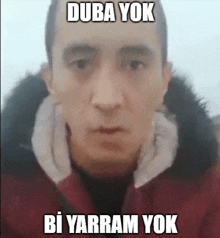 a man in a red jacket is making a funny face and has the words duba yok bi yarram yok written on his face .