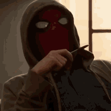 a man wearing a spiderman mask and a hoodie is sitting on a couch holding a cell phone .