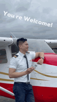 a man in a pilot 's uniform leans against a red and white airplane with the words " you 're welcome " above him