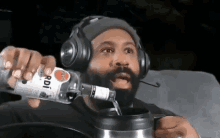 a man with a beard wearing headphones is pouring a bottle of bacardi vodka into a mug .