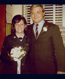 a man and a woman posing for a picture with a bouquet of flowers