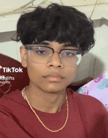 a young man wearing glasses and a gold chain looks at the camera with a tiktok logo in the corner