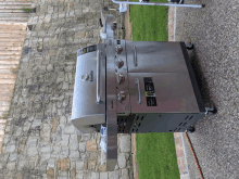 a stainless steel grill is sitting on a gravel driveway next to a stone wall