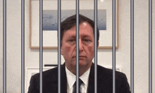 a man in a suit and tie behind bars with a picture on the wall behind him