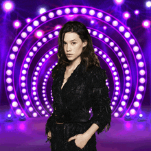 a woman in a black dress is standing in front of a purple background with lights