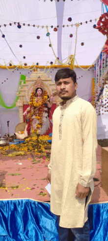 a man in a white kurta stands in front of a statue of a woman