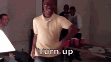 a man in a yellow shirt is dancing in a dark room with the words turn up written on his shirt