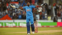 a cricket player is standing on a cricket field holding a bat and a helmet .