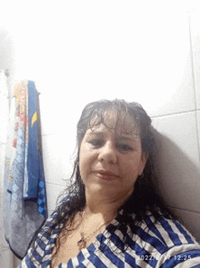 a woman in a blue and white striped shirt is taking a selfie in the bathroom .