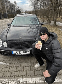 a man is squatting in front of a black mercedes with a license plate that says luz 607