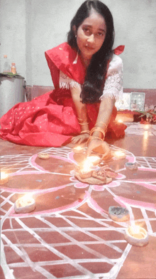 a girl in a red dress is sitting on the floor with candles