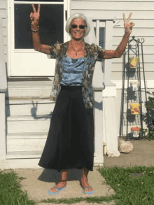 a woman is standing in front of a house giving a peace sign with her arms in the air .