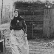 a black and white photo of a woman standing in front of a wooden building with a laurel wreath on it