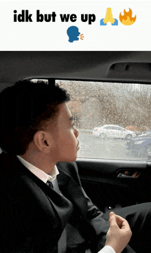 a man in a suit sits in the back seat of a car looking out the window