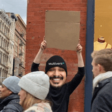 a man wearing a multivers hat holds up a sign