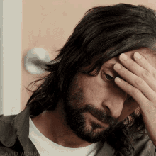 a man with long hair and a beard holds his hand to his forehead in a photo by david worrier