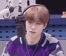 a young man wearing headphones and a purple sweater is sitting in front of a microphone in a radio station .