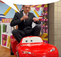 a man in a suit is sitting on a toy car in front of a carnival sign that says fair