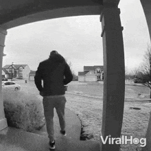 a black and white photo of a man walking in front of a house with viralhog written on the bottom right