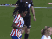 a woman in a red and white striped shirt stands on a soccer field during a game between spa and atl