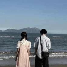 a man and a woman are standing on the beach looking at the ocean