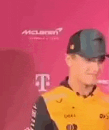 a man wearing a yellow jacket and a baseball cap is standing in front of a pink wall .