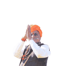 a man wearing an orange turban holds his hands together in a prayer