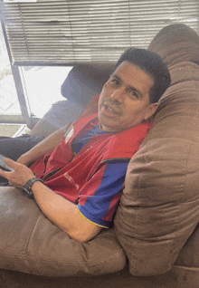 a man is sitting on a couch wearing a red shirt that says ' ralph lauren ' on the front