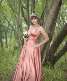 a woman in a pink dress is standing next to a tree