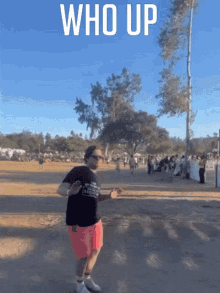 a man in a black shirt and pink shorts is dancing in front of a sign that reads who up