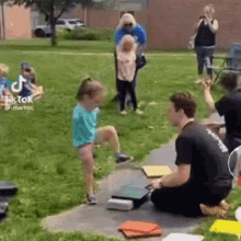 a group of people are sitting on the ground in a park while a little girl is standing in the grass .