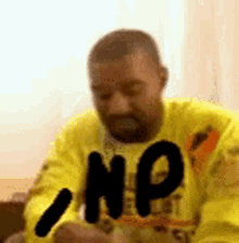 a man wearing a yellow shirt with the word np on it is sitting on a couch .