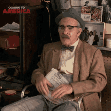 an elderly man sitting in a chair reading a newspaper with coming to america written on the wall behind him