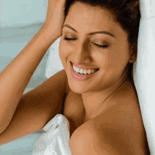 a naked woman is smiling while wrapped in a white towel and smiling with her eyes closed .