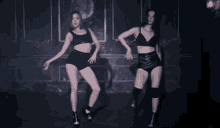 two women are dancing in a dark room with a purple wall behind them